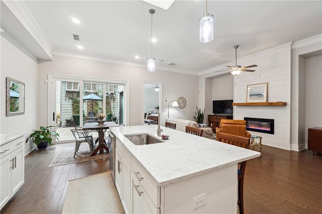 kitchen with sink, white cabinetry, hanging light fixtures, light stone countertops, and a kitchen island with sink