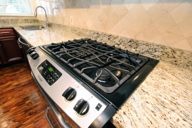 details with light stone counters, a sink, tasteful backsplash, dark wood finished floors, and stainless steel range with gas stovetop