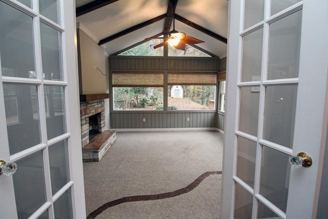 unfurnished sunroom with lofted ceiling with beams, french doors, a stone fireplace, and a ceiling fan