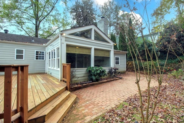 back of house with a deck, a chimney, and a sunroom