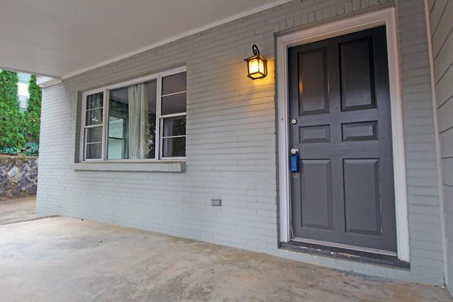 doorway to property featuring covered porch and brick siding