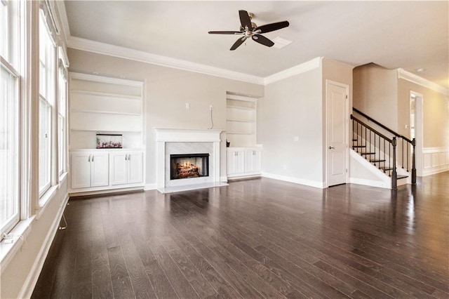 unfurnished living room with stairway, ceiling fan, ornamental molding, dark wood-type flooring, and built in shelves