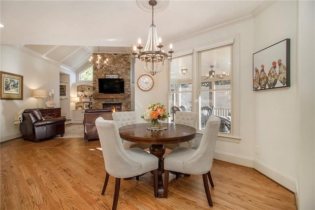 dining area featuring a fireplace, ceiling fan with notable chandelier, light hardwood / wood-style floors, and vaulted ceiling