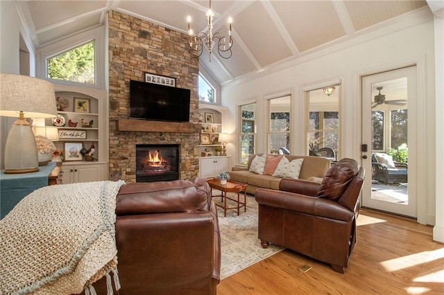 living room featuring high vaulted ceiling, ceiling fan with notable chandelier, a stone fireplace, built in shelves, and light hardwood / wood-style floors