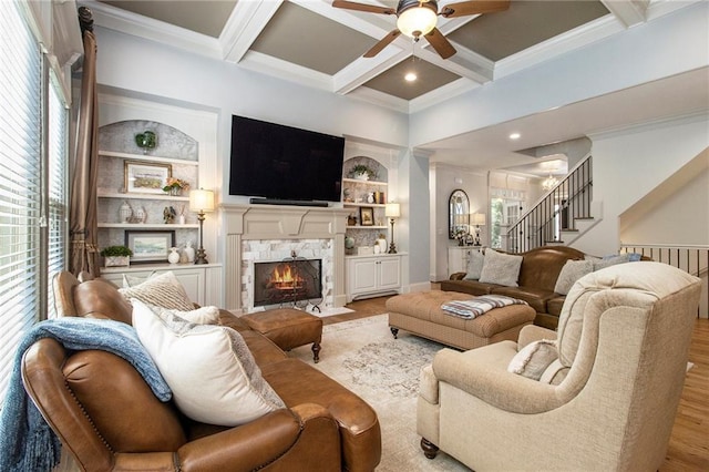 living room with coffered ceiling, built in shelves, beamed ceiling, light hardwood / wood-style floors, and a stone fireplace