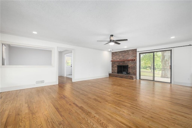 unfurnished living room with crown molding, a textured ceiling, a brick fireplace, light hardwood / wood-style flooring, and ceiling fan