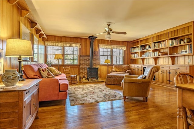 sitting room featuring a wood stove, wooden walls, a ceiling fan, and wood finished floors