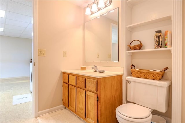 bathroom with baseboards, a drop ceiling, vanity, and toilet