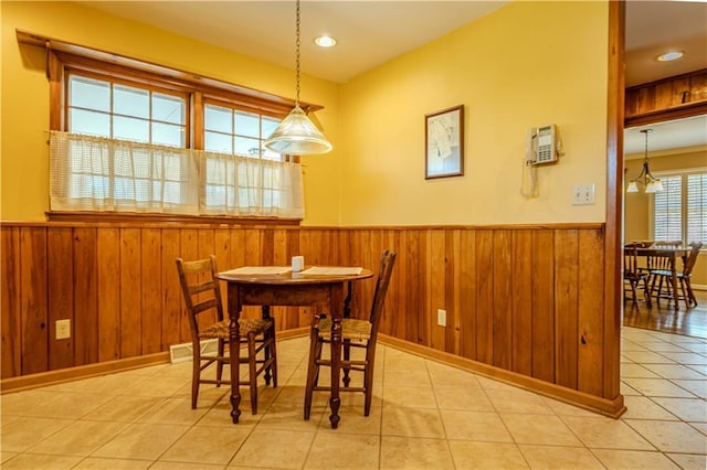 dining space with light tile patterned flooring, wooden walls, visible vents, and wainscoting