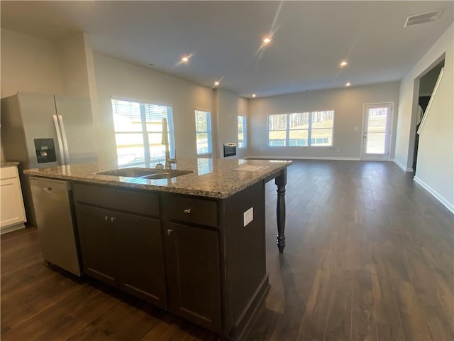 kitchen with dark brown cabinetry, white cabinetry, dishwasher, light stone countertops, and a center island with sink