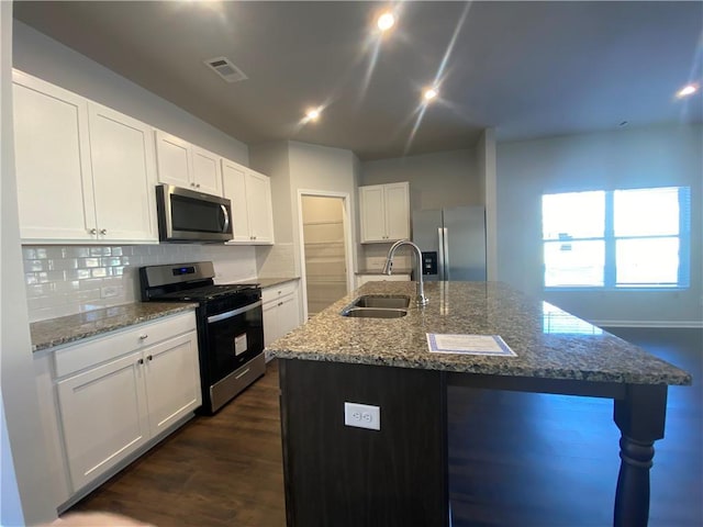 kitchen with stainless steel appliances, sink, stone countertops, white cabinets, and an island with sink