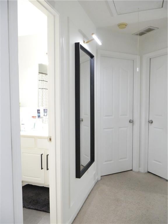 hall featuring visible vents, attic access, and light carpet