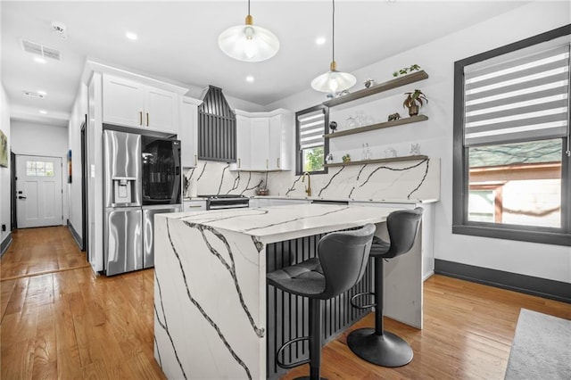 kitchen with a kitchen island, stainless steel fridge with ice dispenser, white cabinets, light wood-style floors, and tasteful backsplash