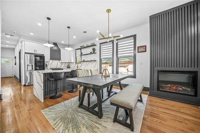 dining space with visible vents, light wood-style flooring, a glass covered fireplace, recessed lighting, and a chandelier