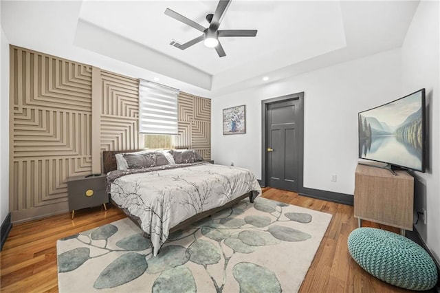 bedroom featuring visible vents, ceiling fan, baseboards, a tray ceiling, and light wood-style floors