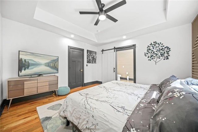 bedroom with baseboards, a barn door, a tray ceiling, wood finished floors, and a ceiling fan