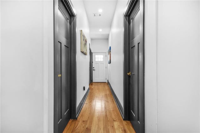 hall featuring visible vents, baseboards, and light wood finished floors