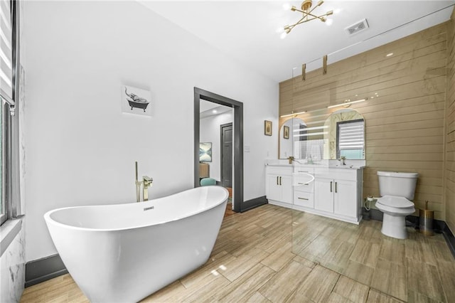 full bath with visible vents, double vanity, a freestanding tub, a sink, and toilet