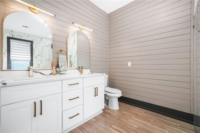 bathroom featuring wood finished floors, visible vents, double vanity, a sink, and toilet