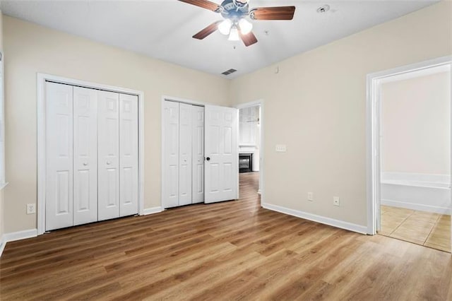 unfurnished bedroom featuring hardwood / wood-style floors, ceiling fan, and multiple closets