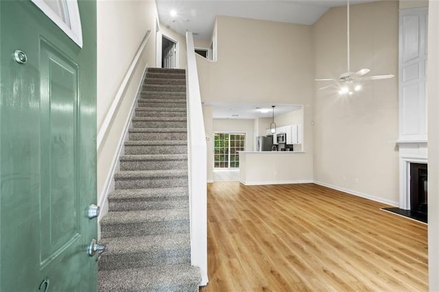 stairway with a high ceiling, ceiling fan, and wood-type flooring