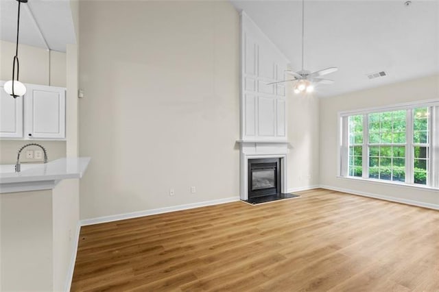 unfurnished living room featuring hardwood / wood-style floors, high vaulted ceiling, sink, ceiling fan, and a large fireplace