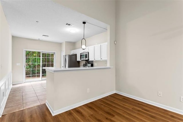 kitchen featuring white cabinets, pendant lighting, stainless steel appliances, and hardwood / wood-style flooring