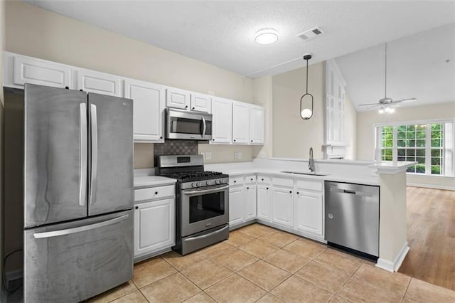 kitchen with white cabinets, sink, vaulted ceiling, appliances with stainless steel finishes, and kitchen peninsula