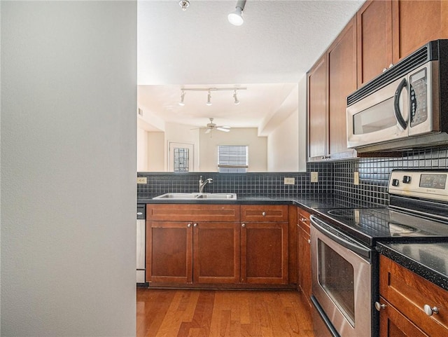 kitchen featuring a sink, decorative backsplash, stainless steel appliances, dark countertops, and light wood-type flooring