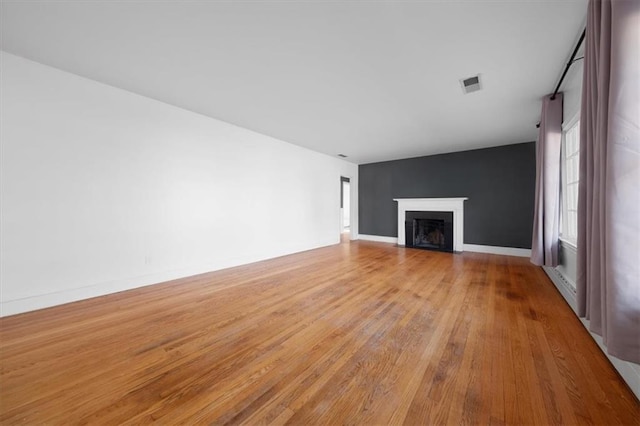 unfurnished living room featuring visible vents, baseboards, a baseboard radiator, a fireplace with flush hearth, and light wood-style flooring