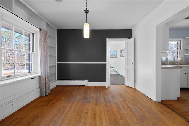 unfurnished dining area with baseboards, built in shelves, baseboard heating, and light wood-style floors