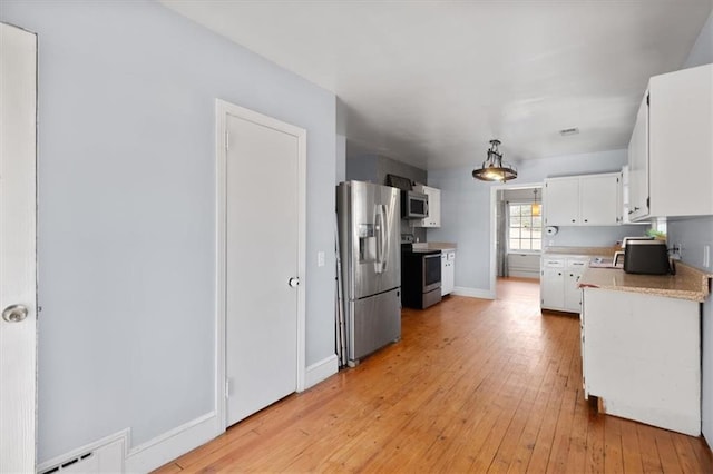 kitchen with white cabinets, appliances with stainless steel finishes, hanging light fixtures, light countertops, and light wood-type flooring