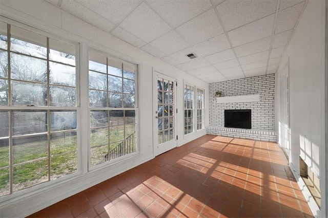 unfurnished sunroom with a fireplace, visible vents, and a drop ceiling