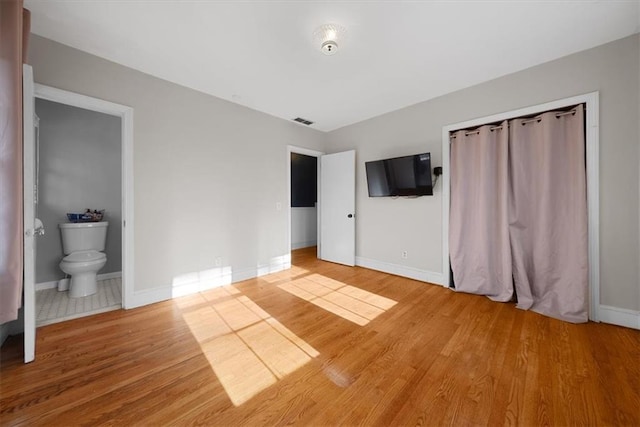 unfurnished bedroom with ensuite bath, wood finished floors, visible vents, and baseboards