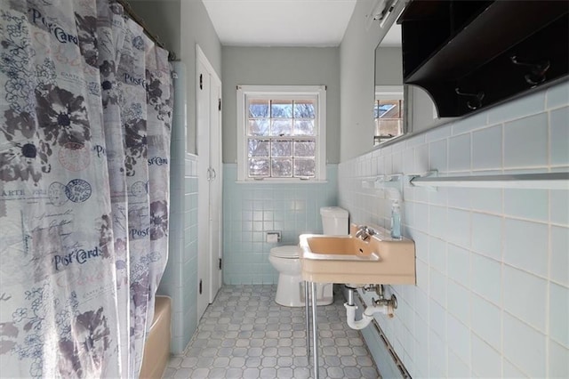 full bath featuring toilet, a wainscoted wall, a sink, and tile walls