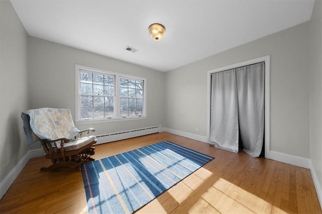 living area featuring a baseboard radiator, wood finished floors, visible vents, and baseboards