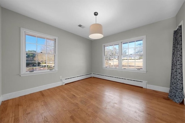 unfurnished room with a baseboard heating unit, wood finished floors, and a healthy amount of sunlight