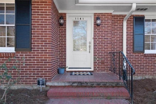 view of exterior entry with visible vents and brick siding