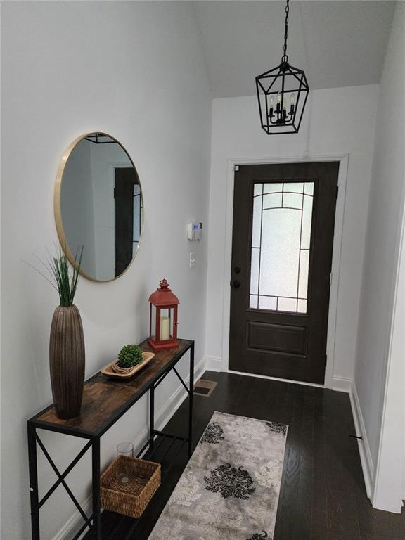 foyer with dark hardwood / wood-style flooring, lofted ceiling, and an inviting chandelier