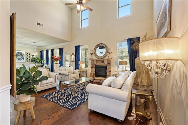 living room featuring ceiling fan with notable chandelier, a stone fireplace, a towering ceiling, dark hardwood / wood-style flooring, and ornamental molding