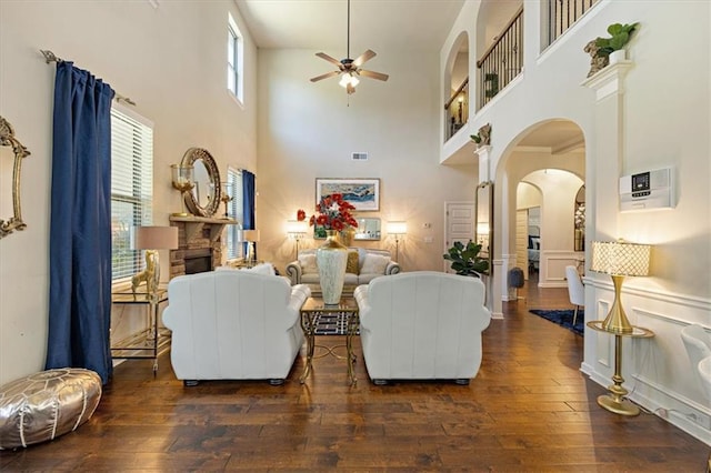 living room with dark hardwood / wood-style floors, a stone fireplace, a towering ceiling, and ceiling fan