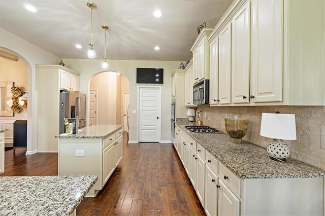 kitchen with appliances with stainless steel finishes, light stone counters, a kitchen island, decorative light fixtures, and dark hardwood / wood-style floors