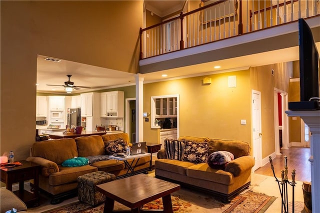 living area with visible vents, light wood-style flooring, a high ceiling, ceiling fan, and ornate columns