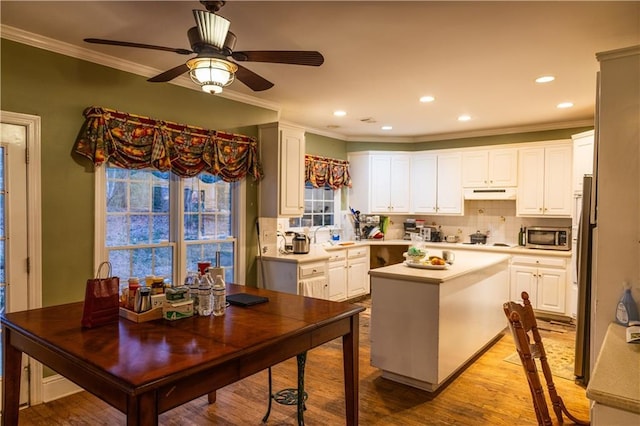 kitchen with under cabinet range hood, stainless steel appliances, a kitchen island, light countertops, and light wood finished floors