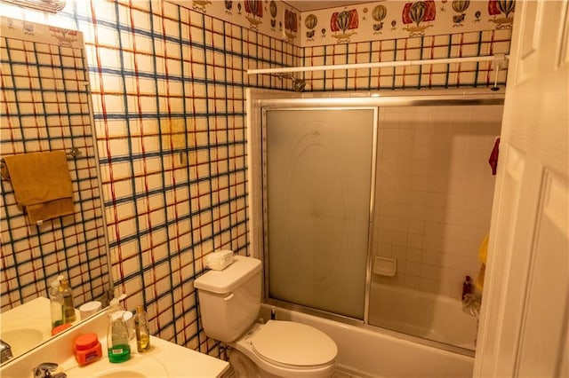 full bath featuring toilet, enclosed tub / shower combo, tile walls, and vanity