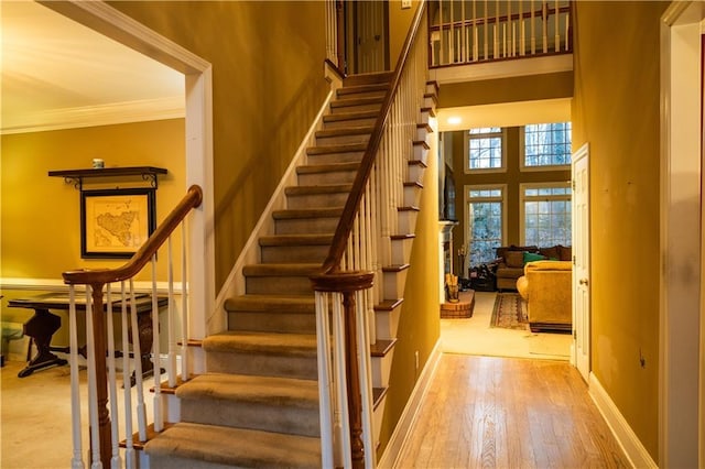 staircase with baseboards, a high ceiling, wood finished floors, and crown molding