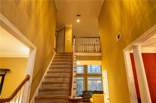 stairway featuring ornamental molding, ornate columns, visible vents, and a high ceiling