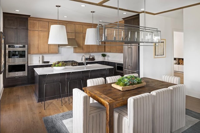 kitchen featuring stainless steel appliances, wood finished floors, a center island with sink, light countertops, and recessed lighting