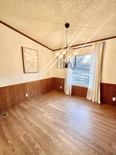 unfurnished dining area with wooden walls, a wainscoted wall, ornamental molding, and a textured ceiling