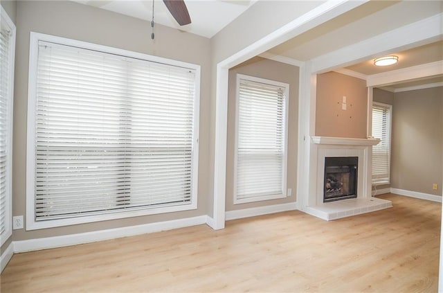 unfurnished living room featuring a fireplace with raised hearth, ceiling fan, wood finished floors, baseboards, and crown molding